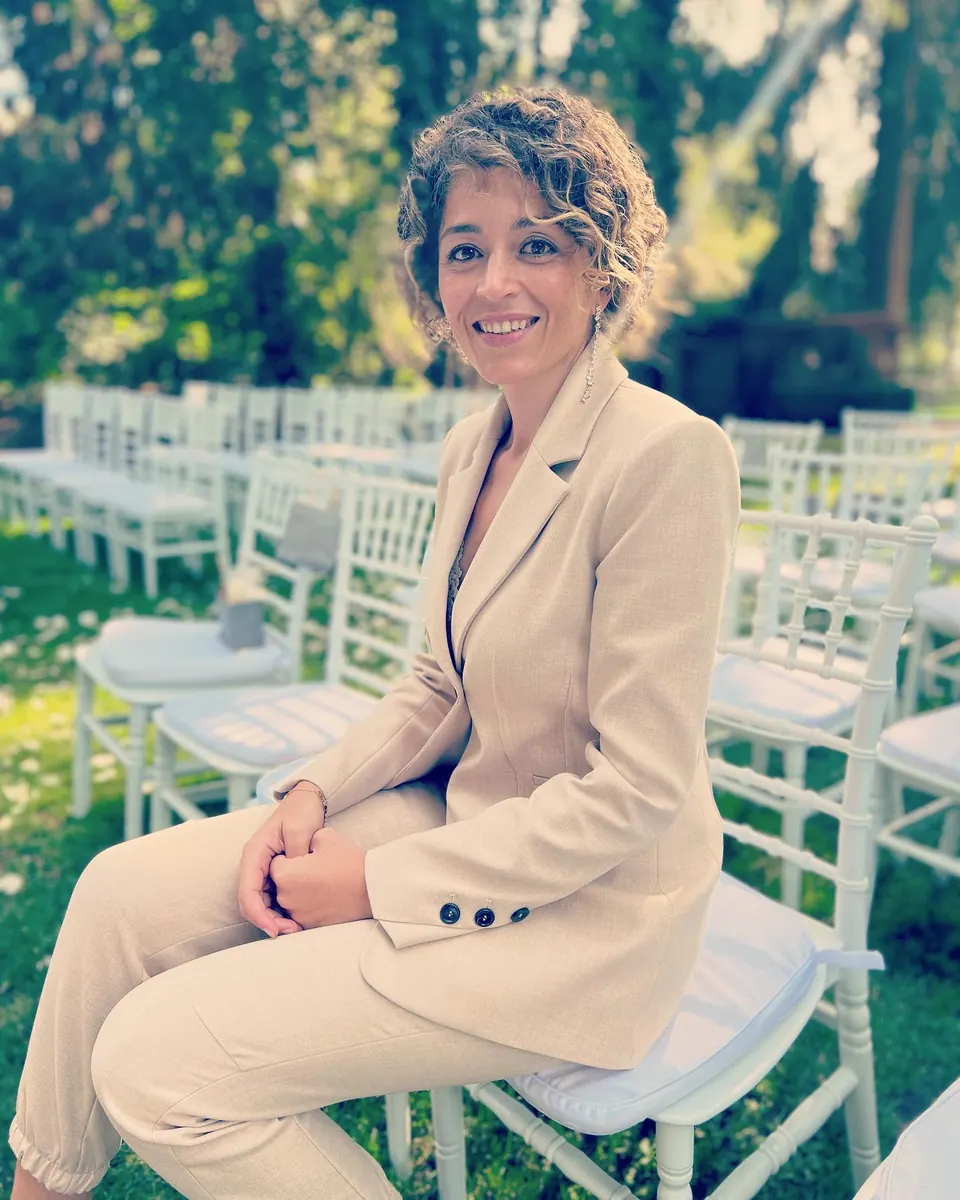 Ximena smiling towards the camera in a light suit, seated among white ceremony chairs