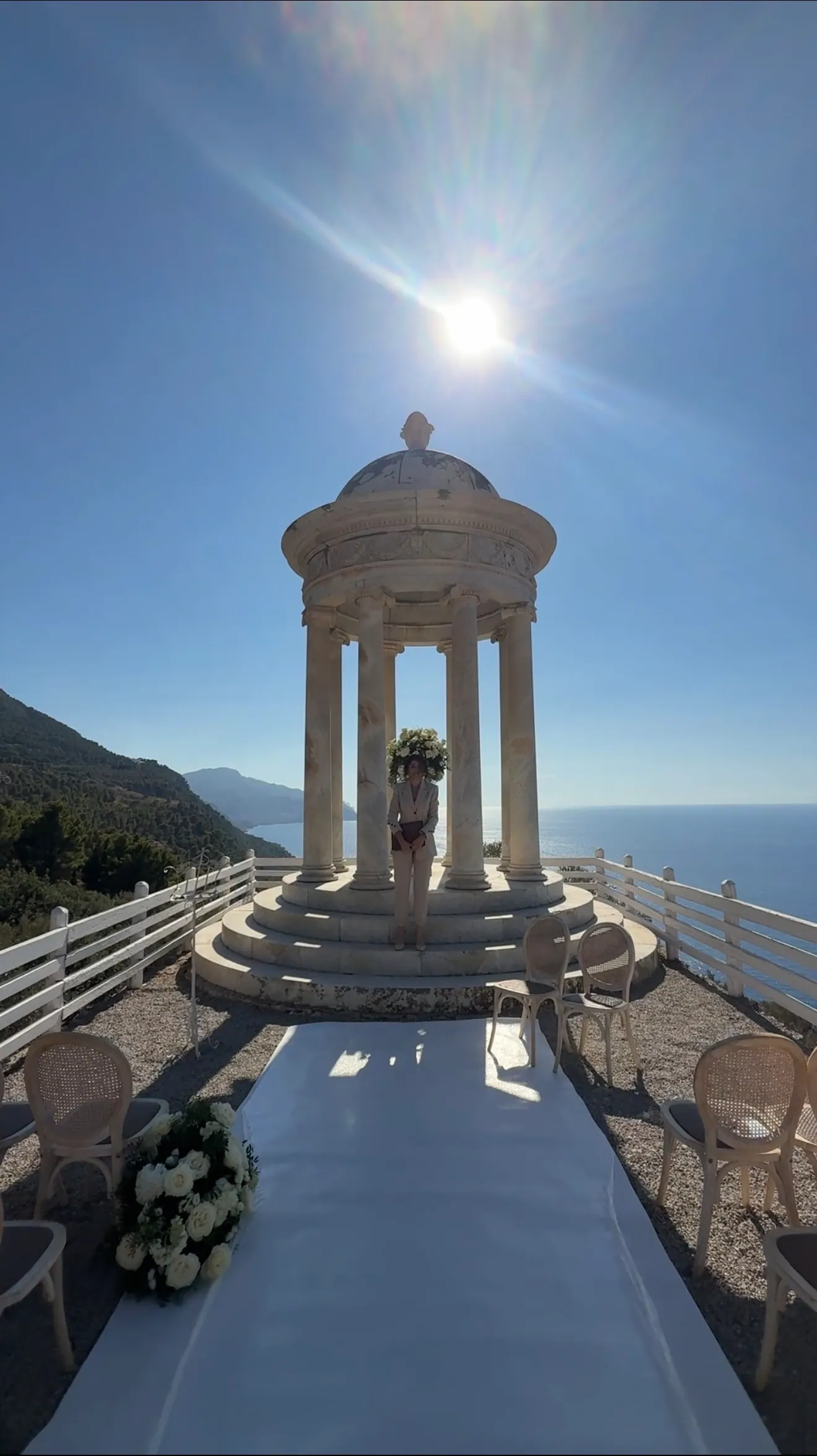 An open-air ceremony setting with a stone pavilion overlooking the water