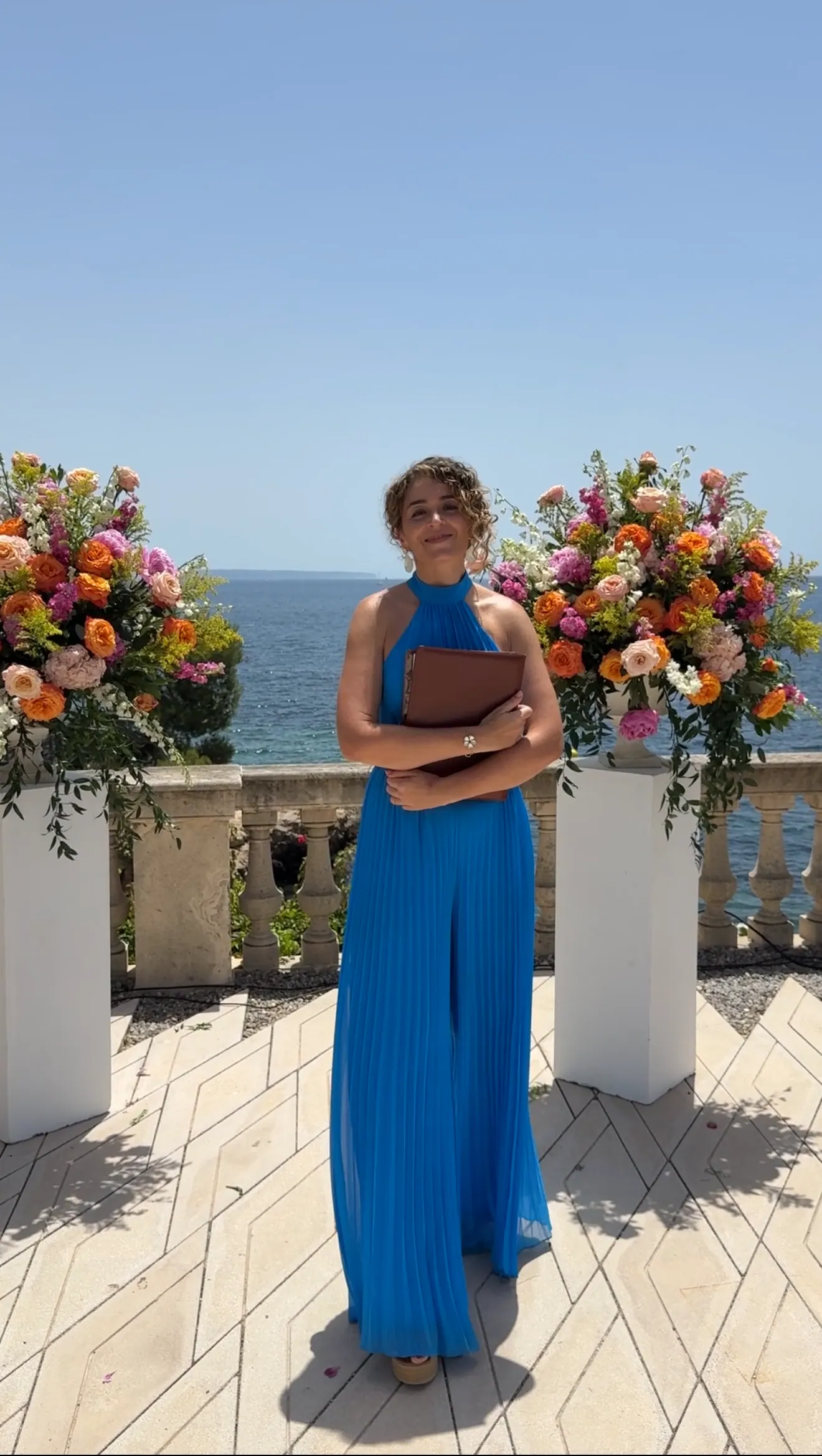 Ximena smiling with her ceremony book between flowers beside the water