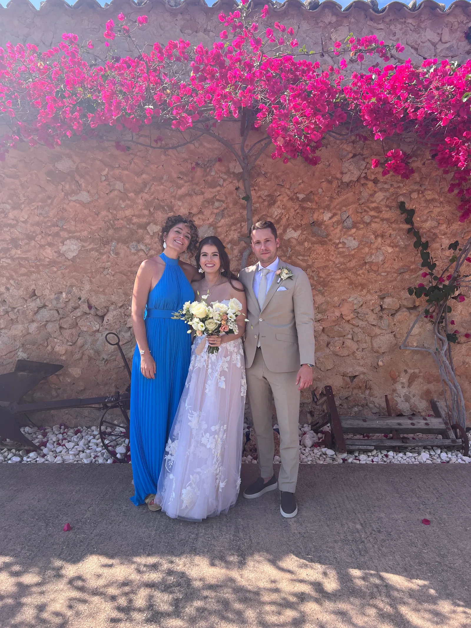 A couple standing with Ximena beneath pink bougainvillea flowers