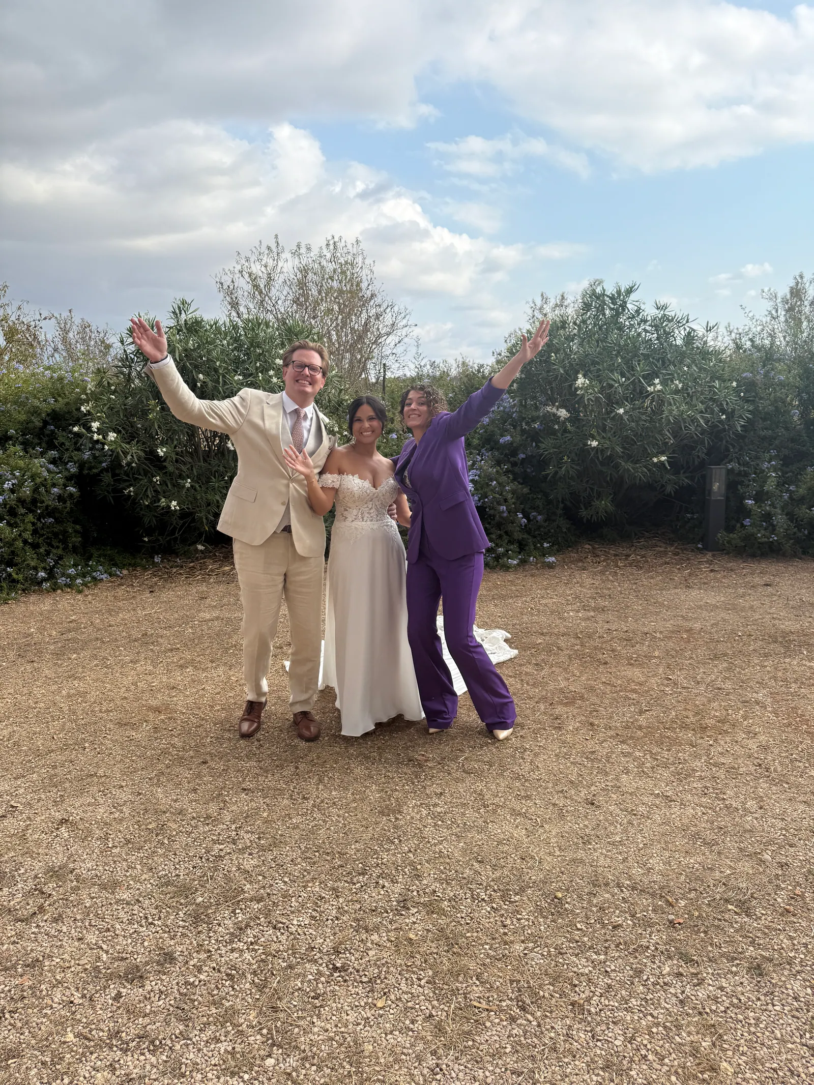 A couple and Ximena raising their arms together in an outdoor wedding setting
