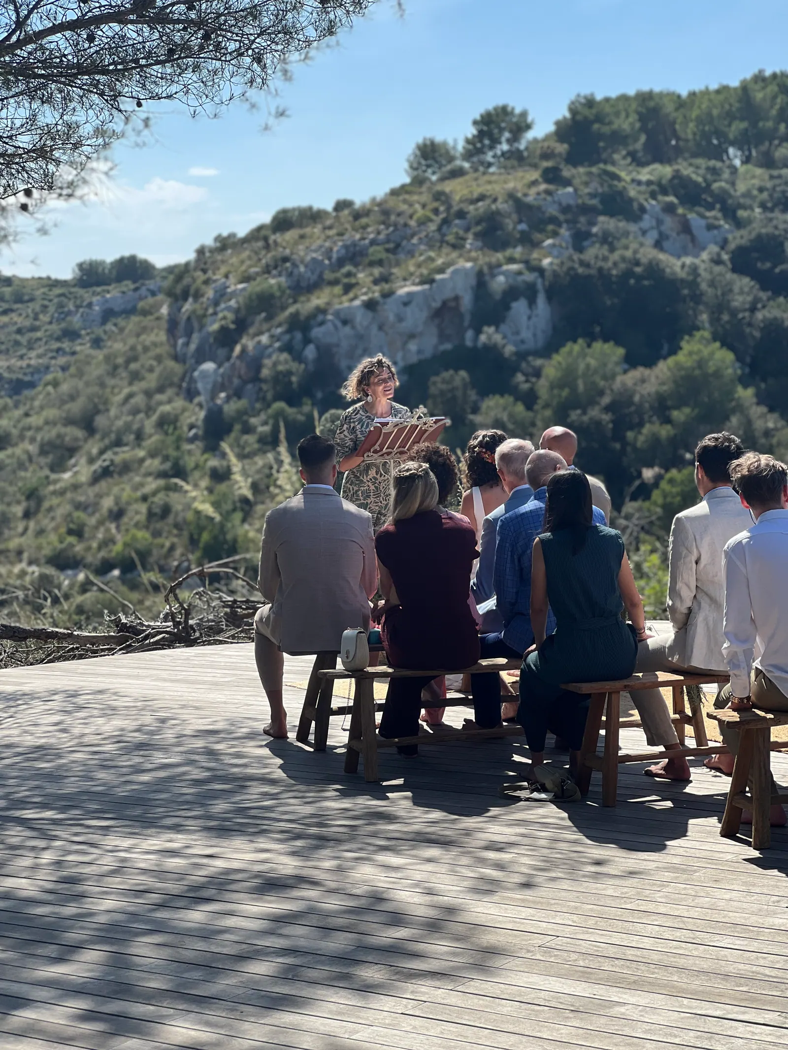 Ximena leading an outdoor ceremony with the couple and their seated guests beneath a tree