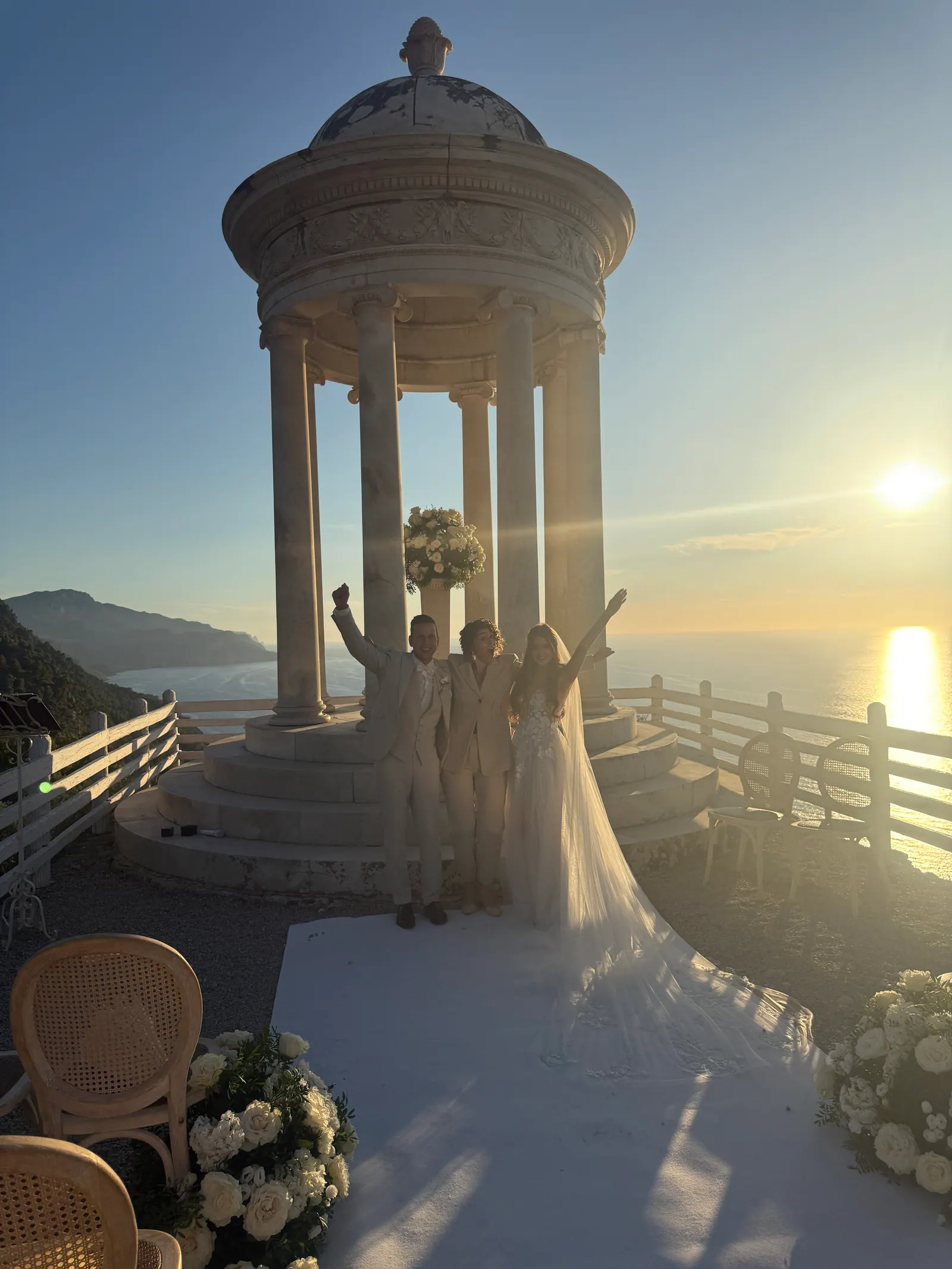 Warm evening light falling across a stone pavilion prepared for a ceremony beside the water