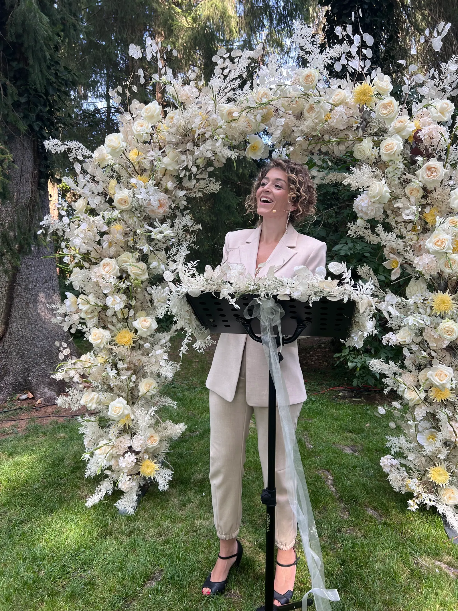 Ximena laughing while speaking beneath an arch of white flowers