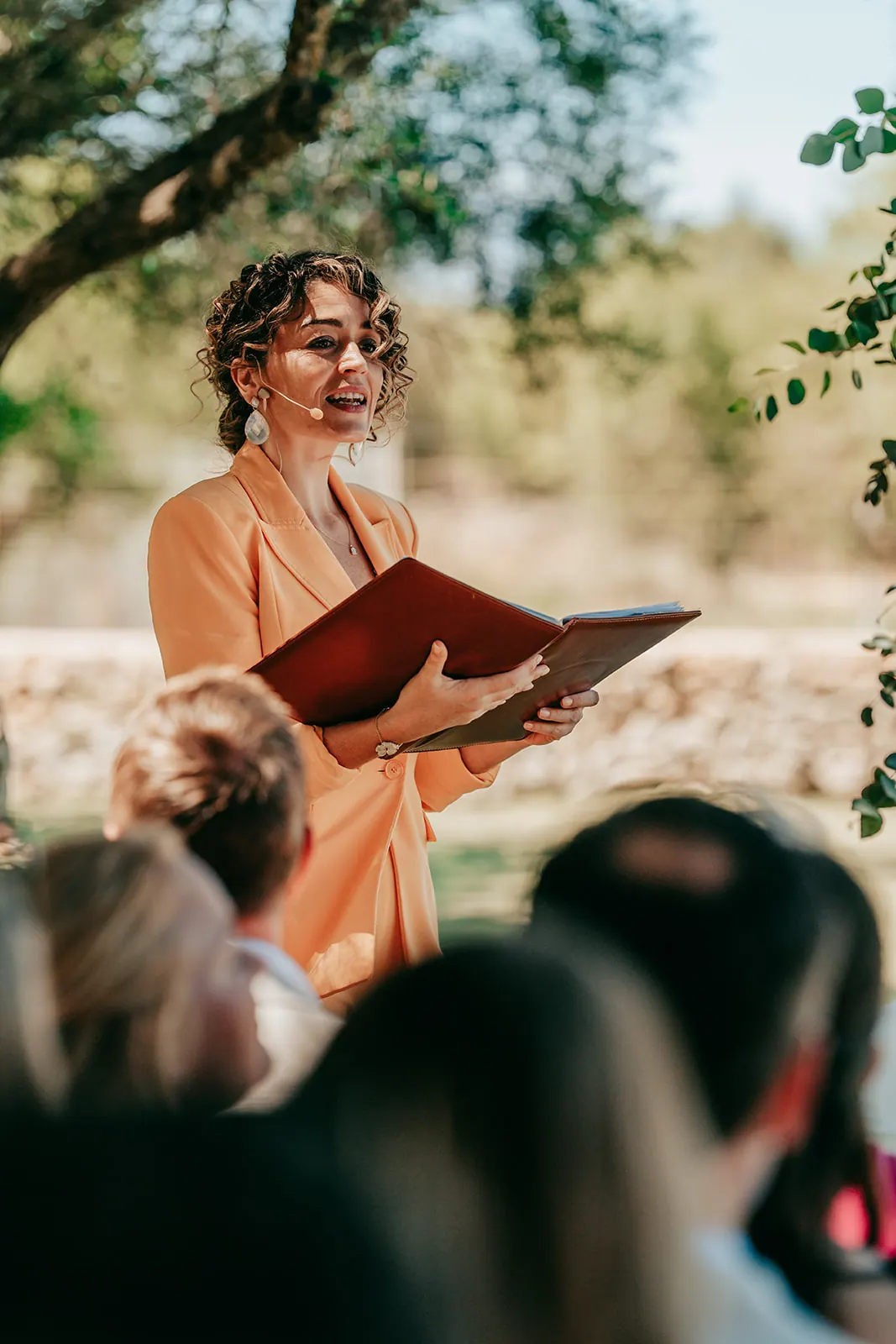 Ximena speaking with a smile and an open ceremony book while guests listen