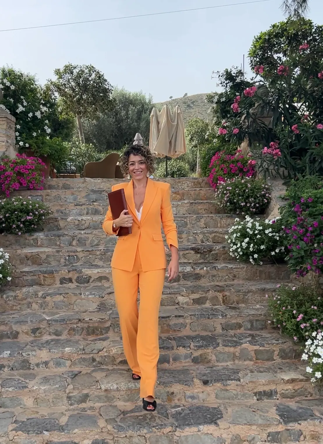 Ximena holding her ceremony book while walking down stone steps beside flowering plants
