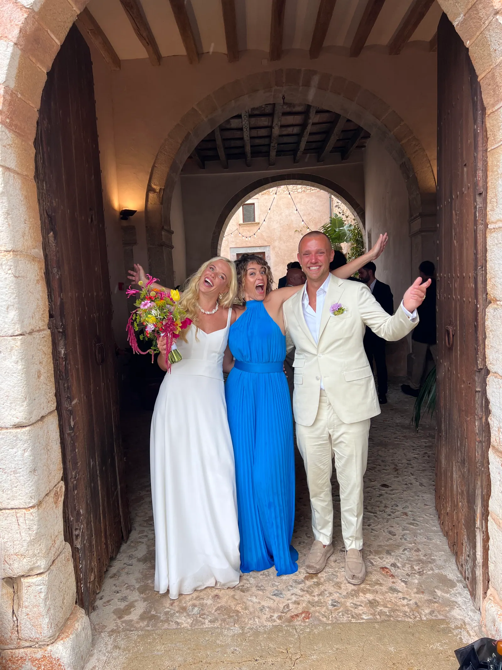 A couple smiling with Ximena in a stone doorway after their ceremony